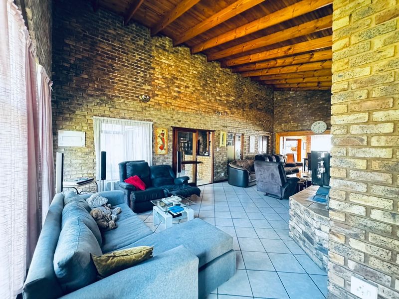 Spacious living area featuring high exposed timber beam ceilings, rustic exposed brick walls, tiled flooring, and a stone-clad fireplace base.