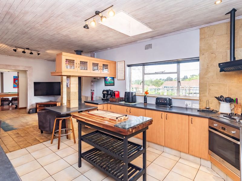 Open-plan kitchen featuring timber ceilings, a skylight, built-in cabinetry, and a breakfast bar, seamlessly flowing into the adjacent living area.