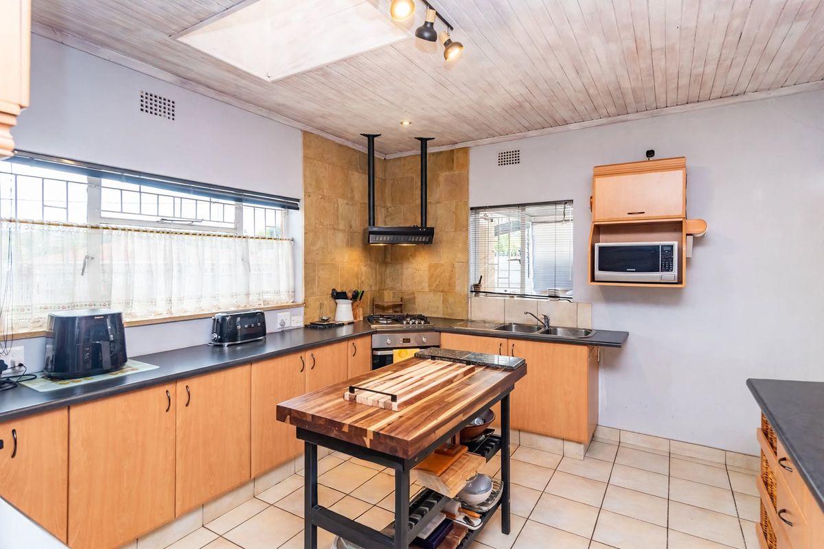 Functional kitchen featuring light wood cabinetry, dark countertops, gas hob with extractor, tiled flooring, and a timber ceiling with a skylight.