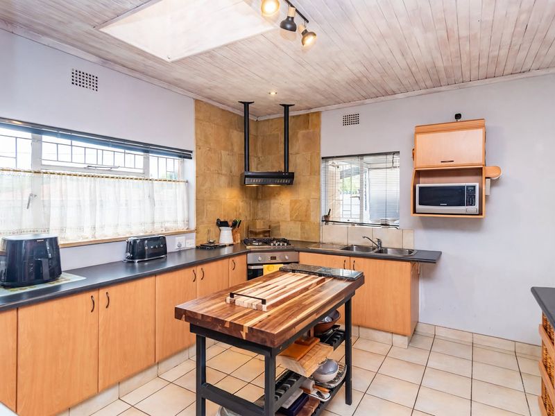 Functional kitchen featuring light wood cabinetry, dark countertops, gas hob with extractor, tiled flooring, and a timber ceiling with a skylight.