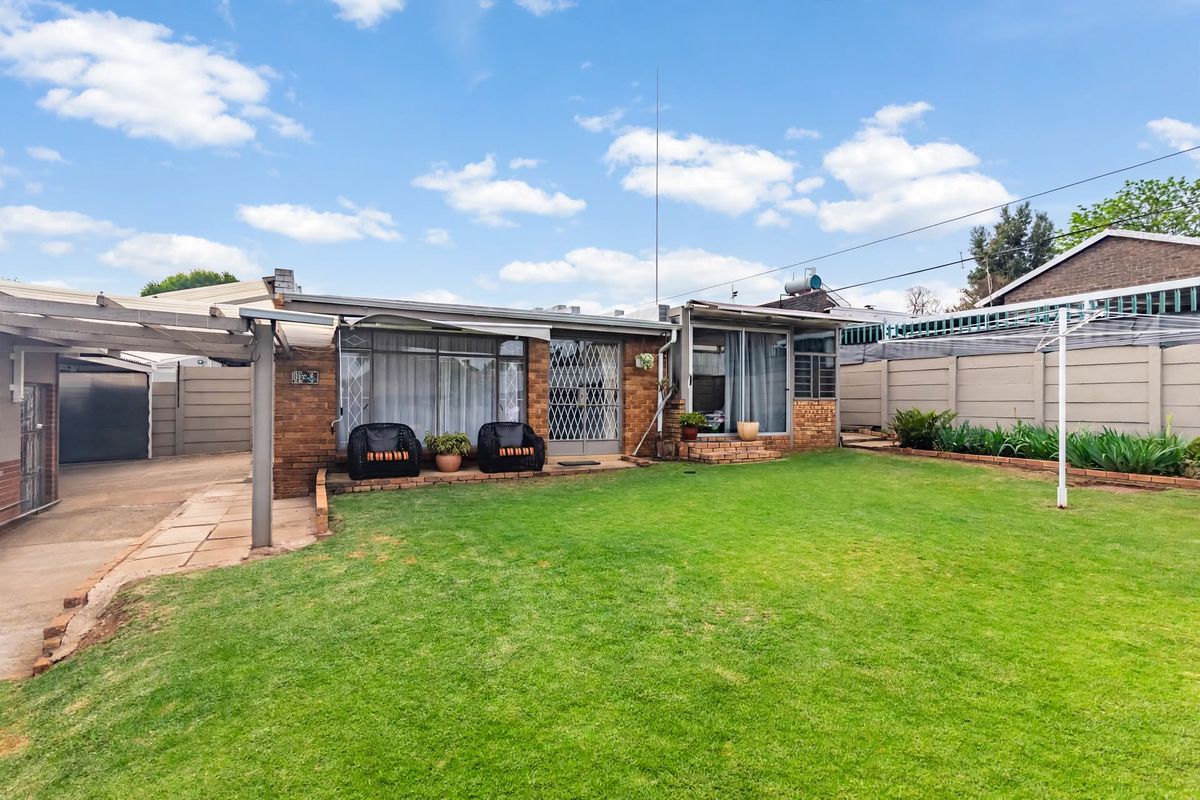 Rear view of the property featuring a brick facade, sliding doors with security gates, a carport, and a well-maintained lawn with perimeter walling.