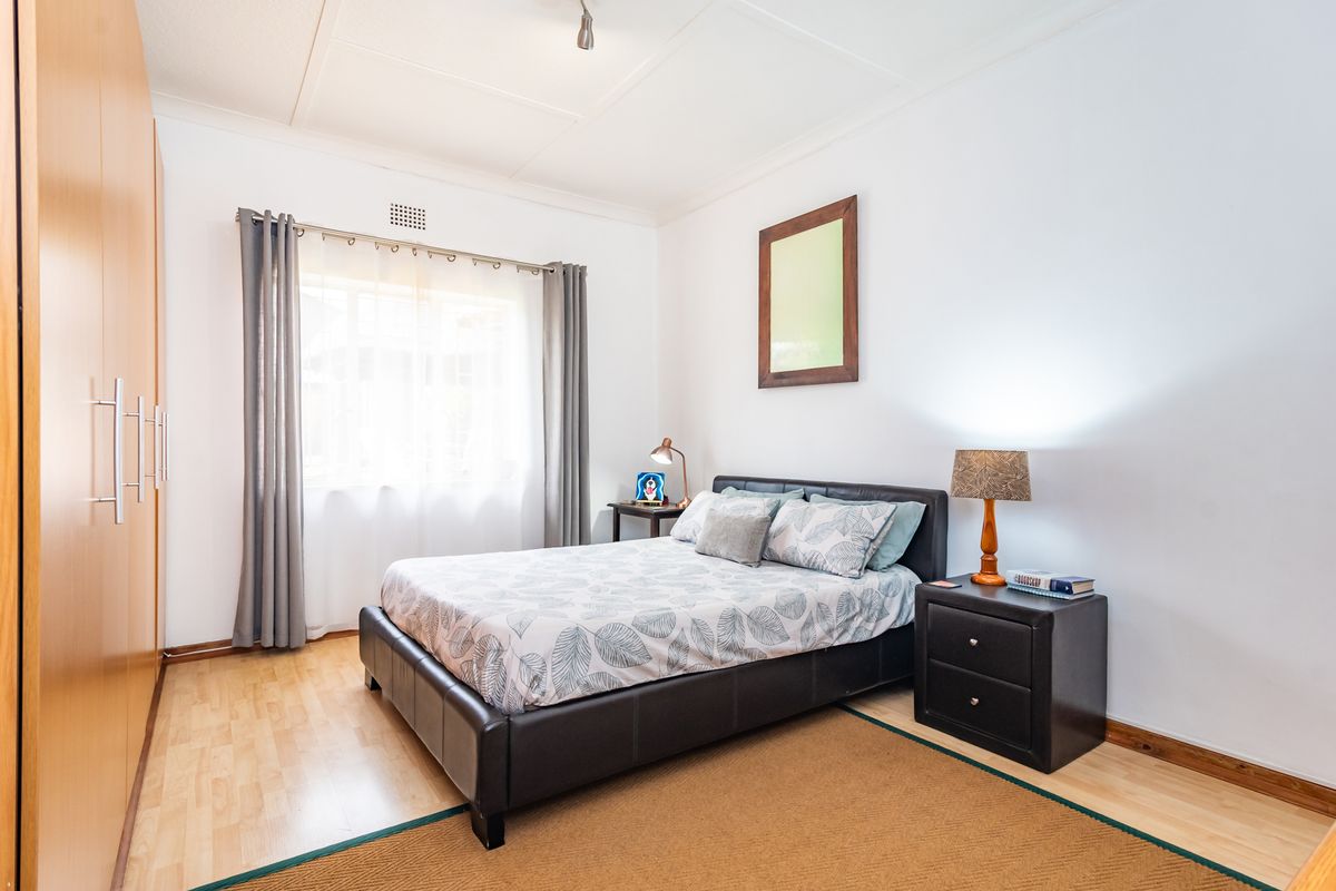 A well-maintained bedroom featuring light laminate flooring, a large built-in wardrobe, and neutral wall finishes.