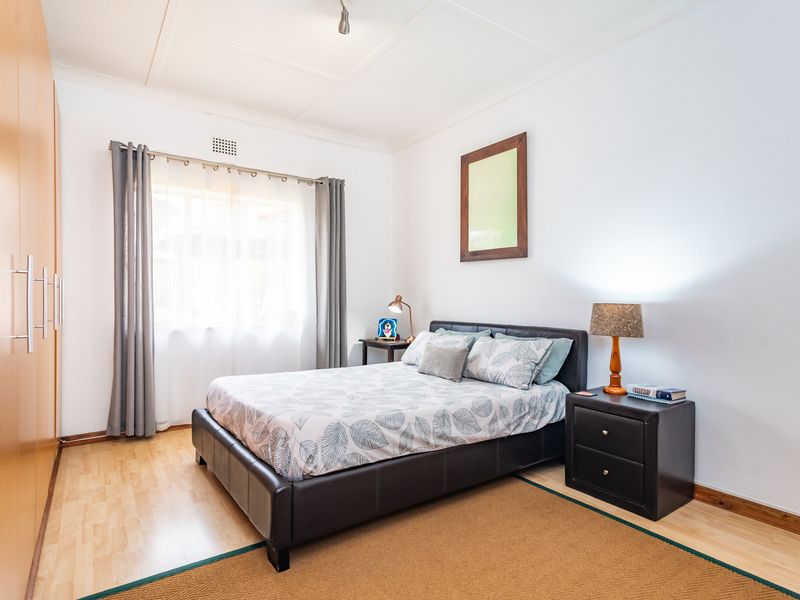 A well-maintained bedroom featuring light laminate flooring, a large built-in wardrobe, and neutral wall finishes.