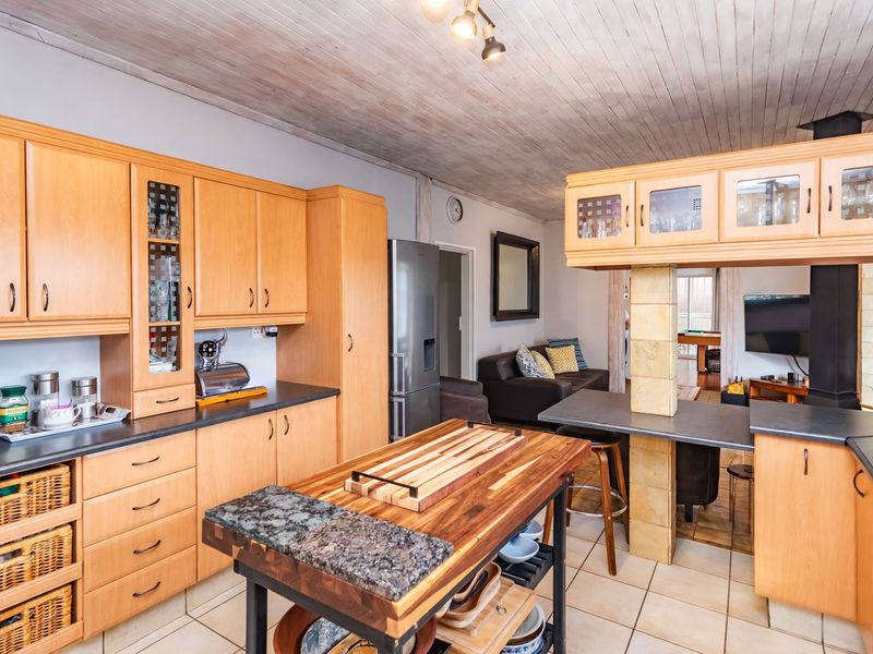 Open plan kitchen featuring light wood cabinetry, stone-topped breakfast bar, and tiled flooring, seamlessly flowing into the adjacent living area with a fireplace.
