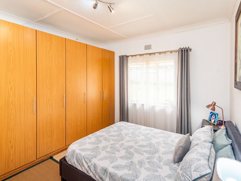 A well-maintained bedroom featuring extensive built-in wooden cupboards, neutral walls, and a window with curtain fixtures.