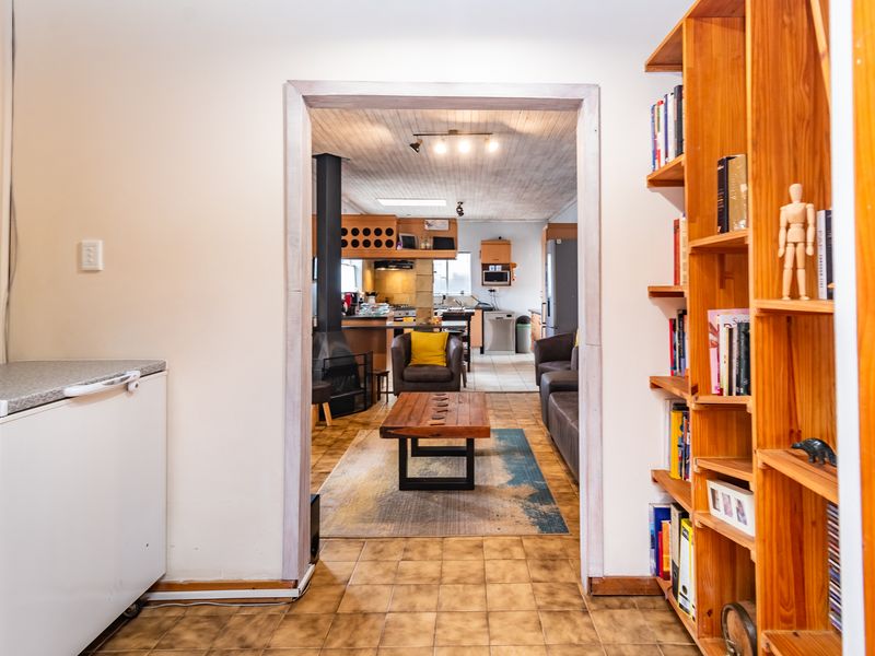 An open-plan living and kitchen area featuring a wood-burning fireplace, tiled flooring, and a timber ceiling, viewed through a doorway with built-in shelving.