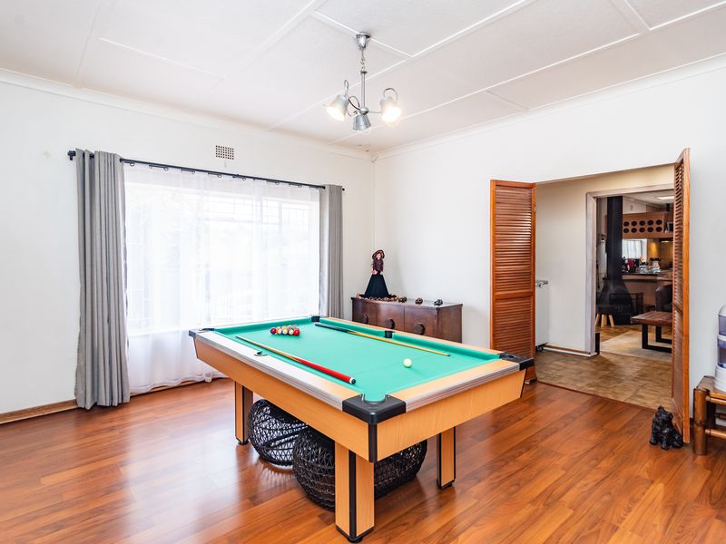 Spacious living area featuring laminate flooring, large window with curtains, and louvered doors leading to an adjacent room.