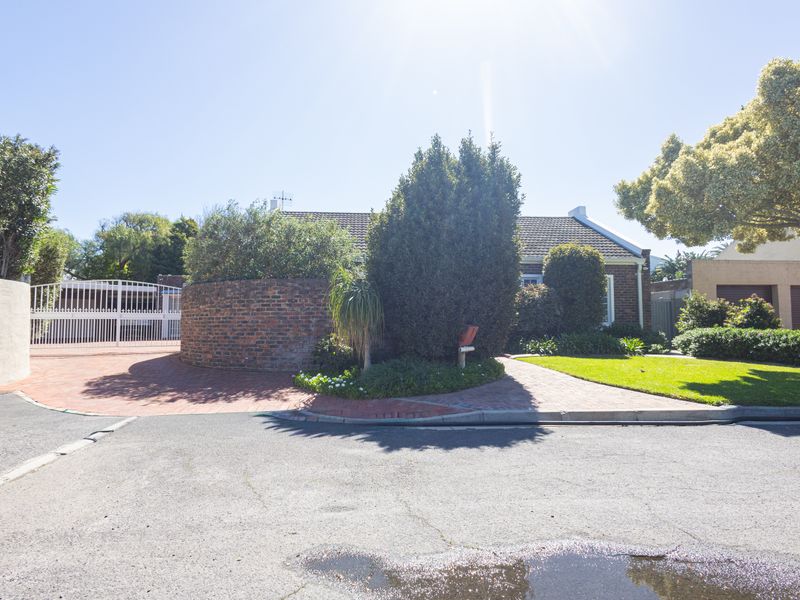 Front view of the property featuring a brick driveway, established garden, and secure gated entrance with a classic brick facade.
