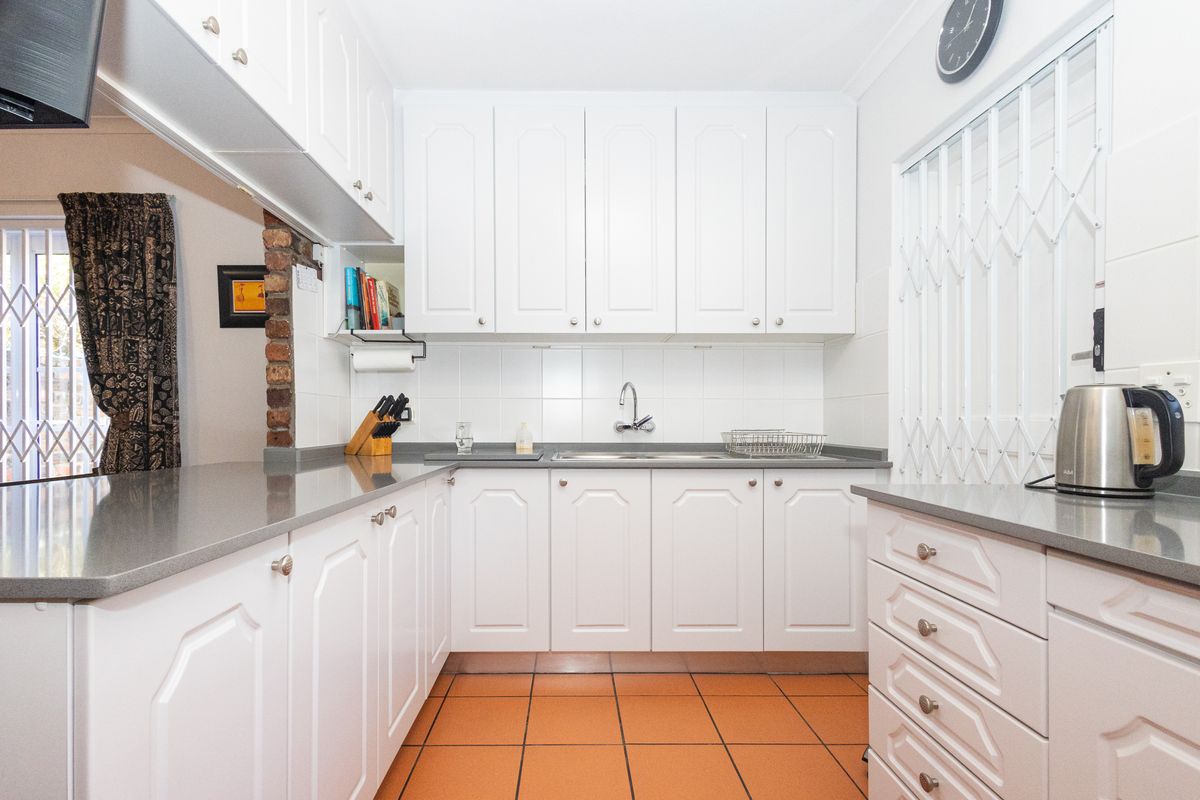 A functional kitchen featuring white cabinetry, grey stone countertops, tiled flooring, and a stainless steel sink with a tiled backsplash.