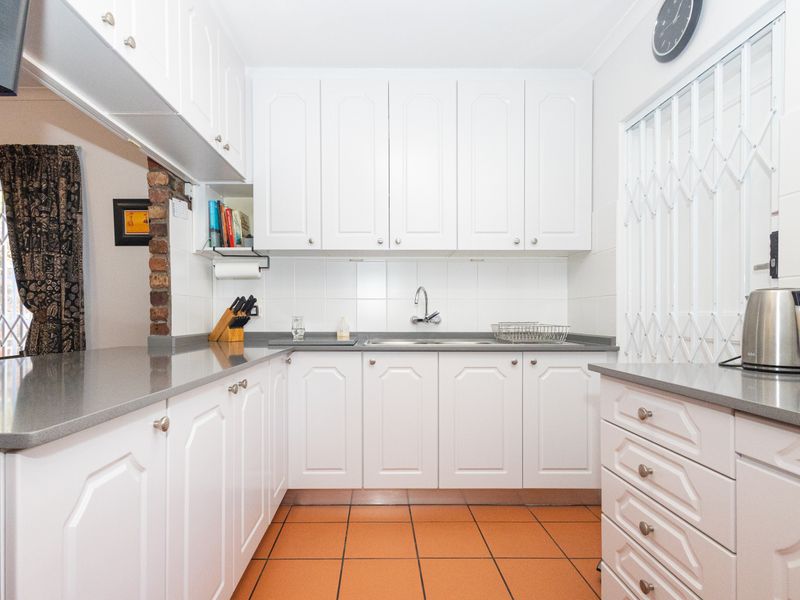A functional kitchen featuring white cabinetry, grey stone countertops, tiled flooring, and a stainless steel sink with a tiled backsplash.