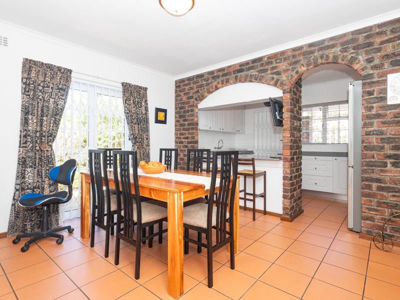 Open plan dining area featuring ceramic floor tiles and a distinctive exposed brick archway leading into a functional kitchen space.