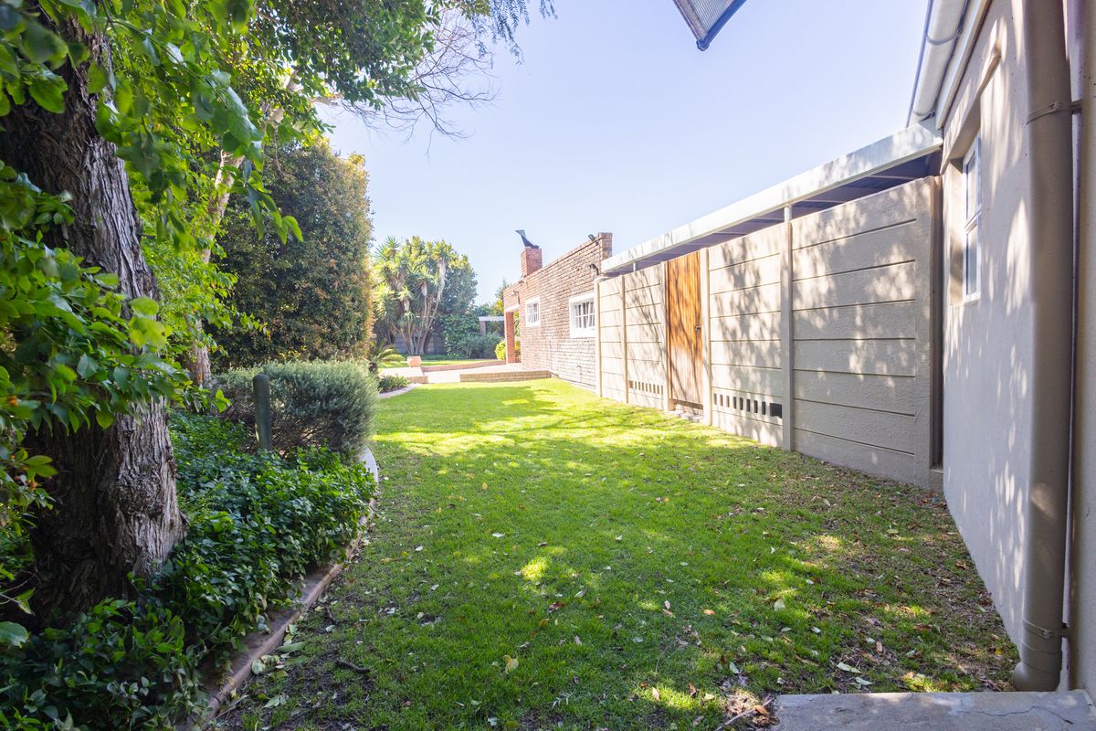 A view of the rear garden featuring a well-maintained lawn, mature trees, and a precast concrete boundary wall alongside the brick exterior of the house.