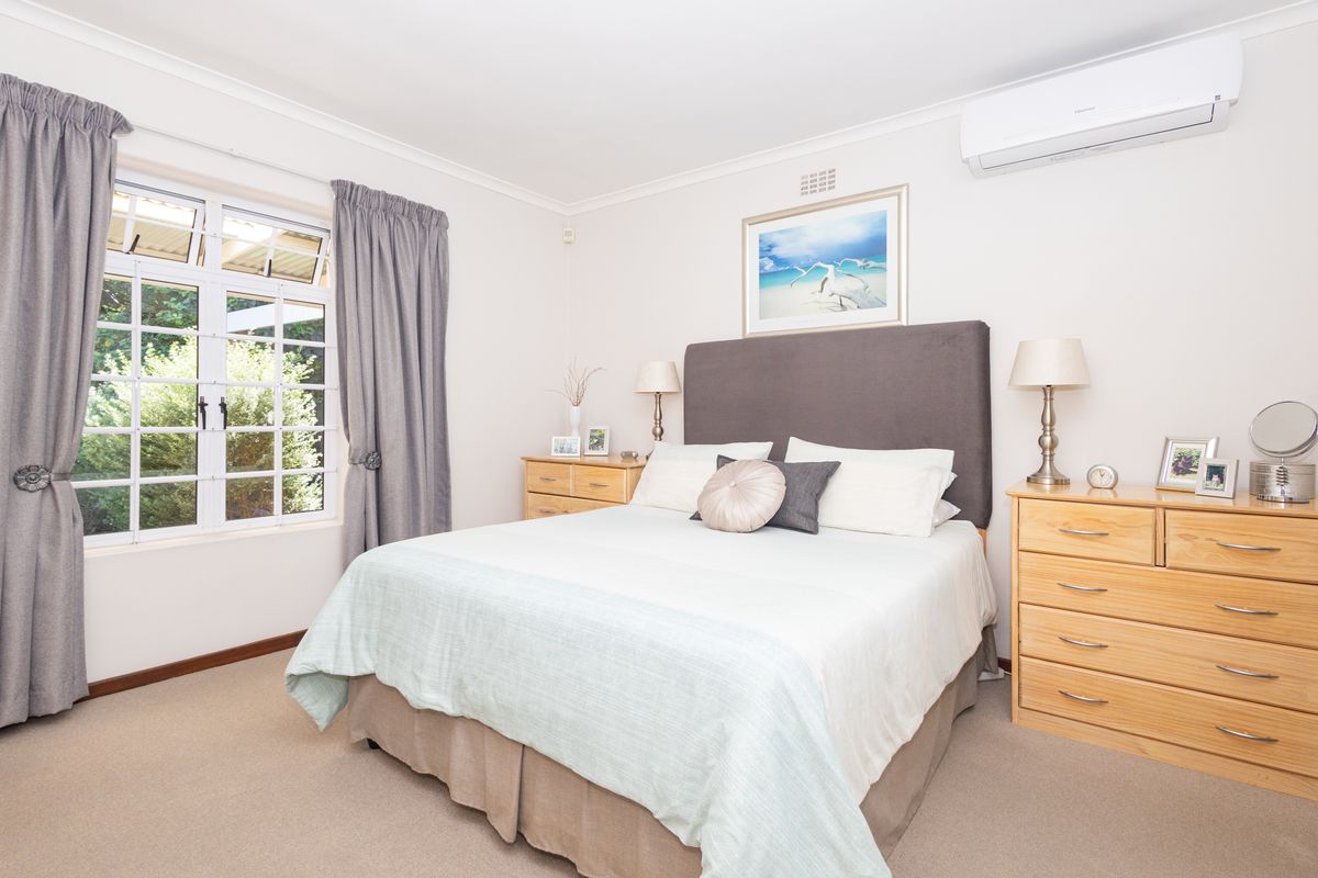 A well-maintained bedroom featuring neutral carpet, a split-system air conditioner, and a large casement window providing natural light.