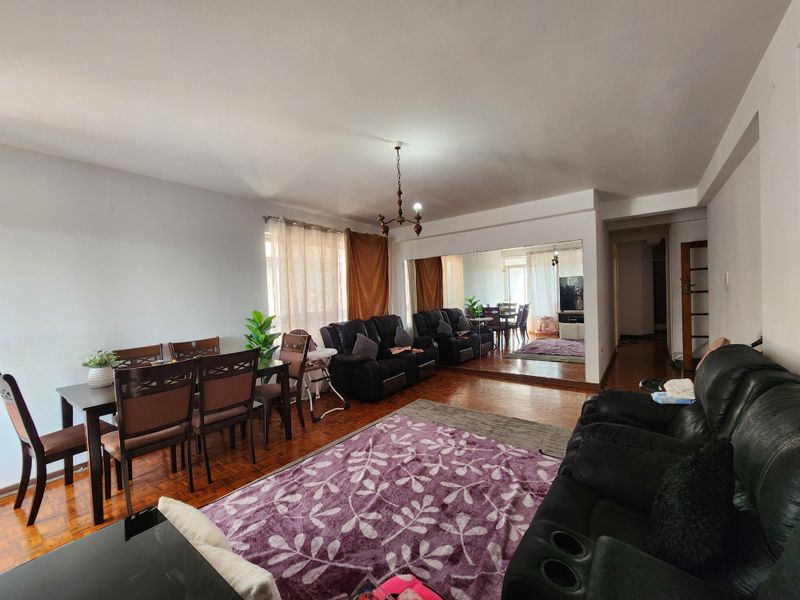 Spacious open-plan living and dining area featuring warm parquet flooring and a large mirrored wall, creating a bright and versatile living space.