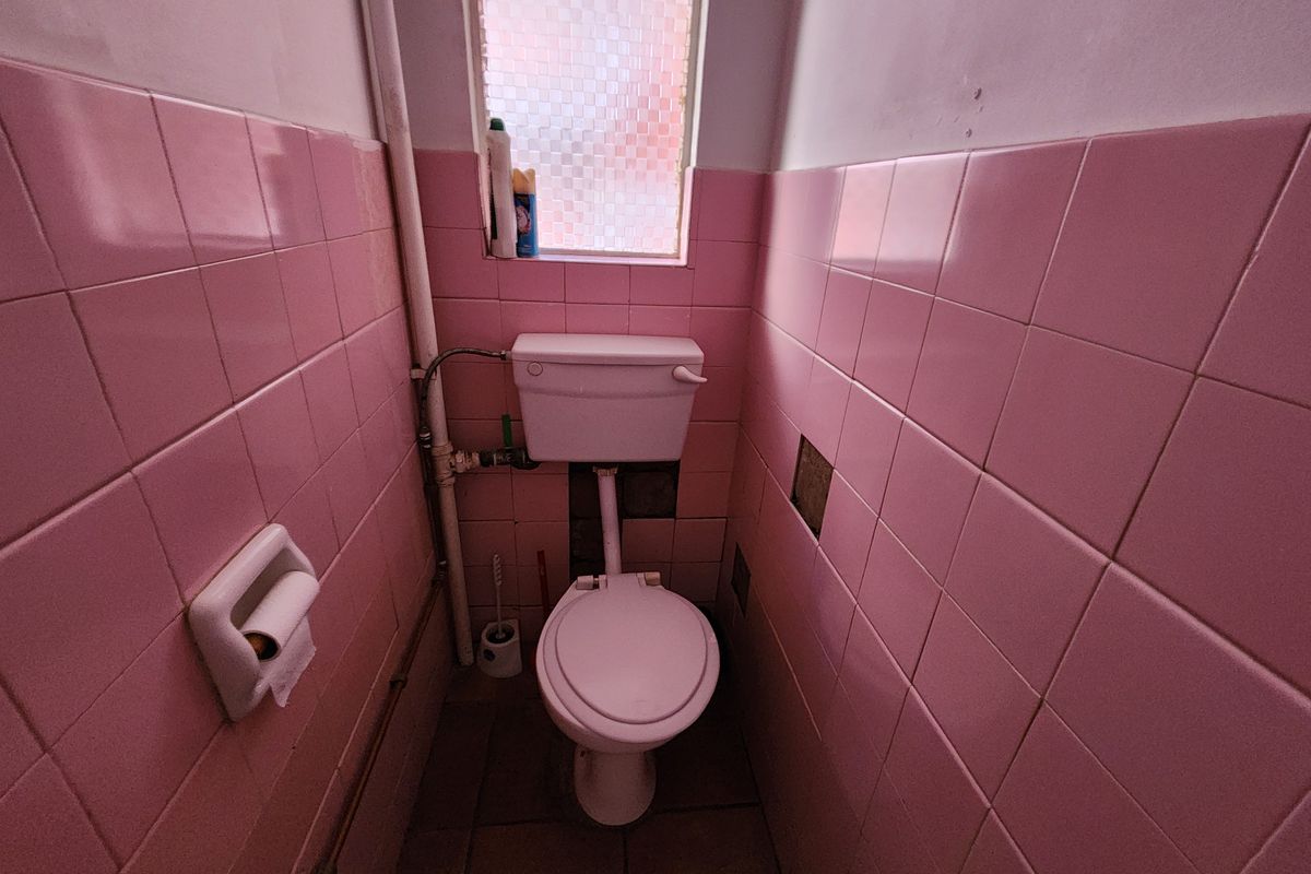 A compact bathroom featuring dated pink wall tiles, a standard toilet, and an obscured glass window, requiring modernization and cosmetic updates.