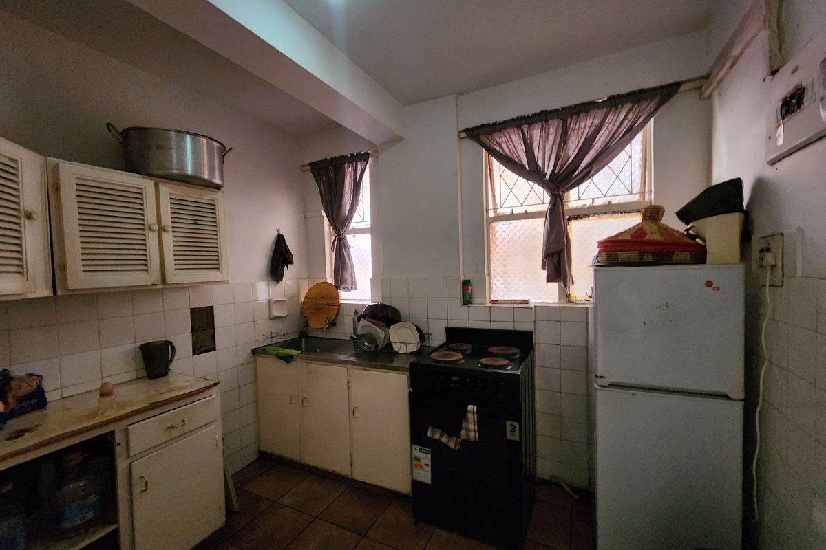A functional kitchen featuring built-in cabinetry, a stainless steel sink, and a freestanding stove, with tiled splashbacks and flooring throughout.