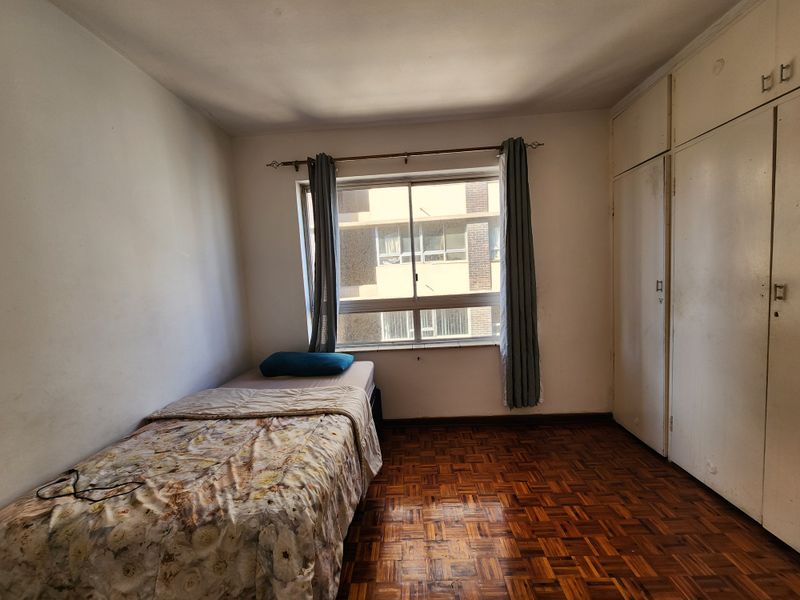 A bedroom featuring classic parquet flooring, built-in storage cupboards, and a window providing natural light.