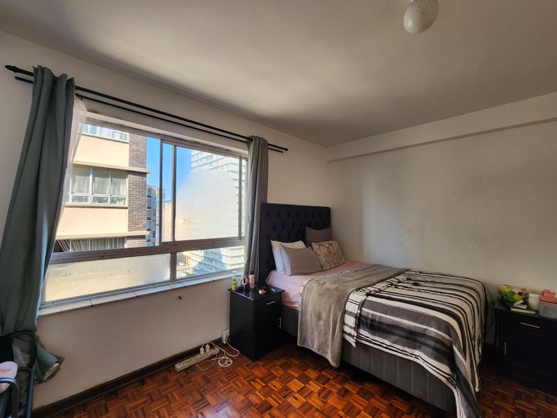 A bedroom featuring classic parquet flooring and a large sliding window, offering natural light and urban views.