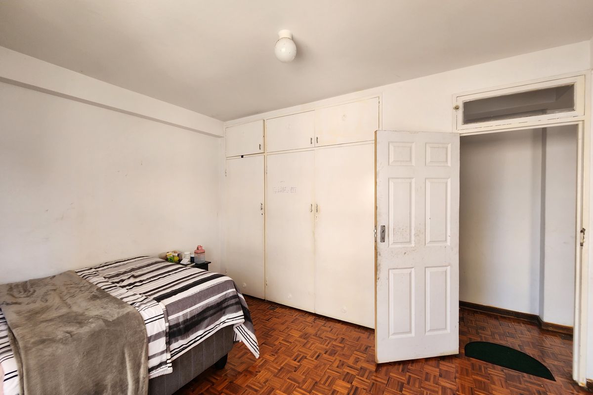 A bedroom featuring original parquet flooring, built-in cupboards, and a classic panel door with a transom window above.