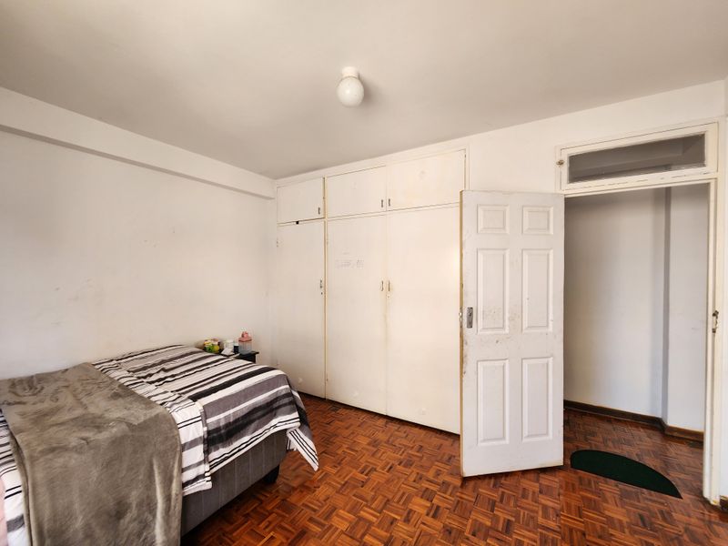 A bedroom featuring original parquet flooring, built-in cupboards, and a classic panel door with a transom window above.