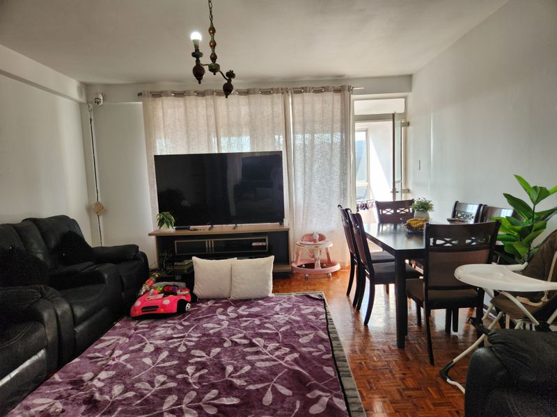 Open plan living and dining area featuring classic parquet flooring and direct access to an outdoor balcony through a sliding glass door.