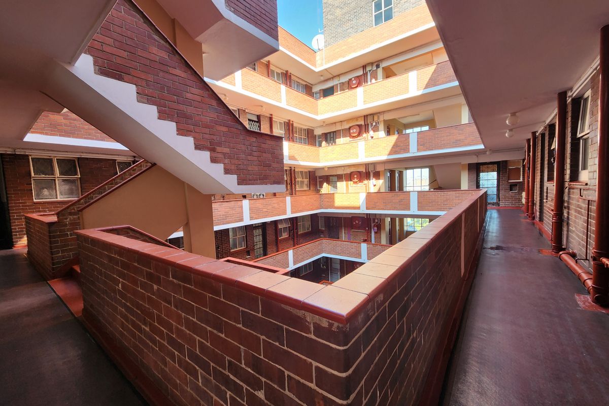 An open-air central atrium and communal walkway area featuring exposed brickwork and stairwell access within an apartment complex.