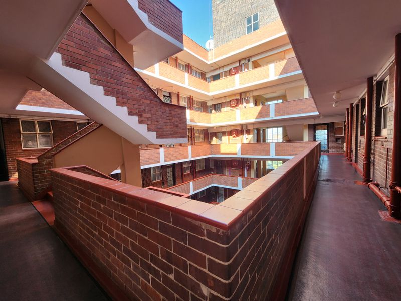 An open-air central atrium and communal walkway area featuring exposed brickwork and stairwell access within an apartment complex.