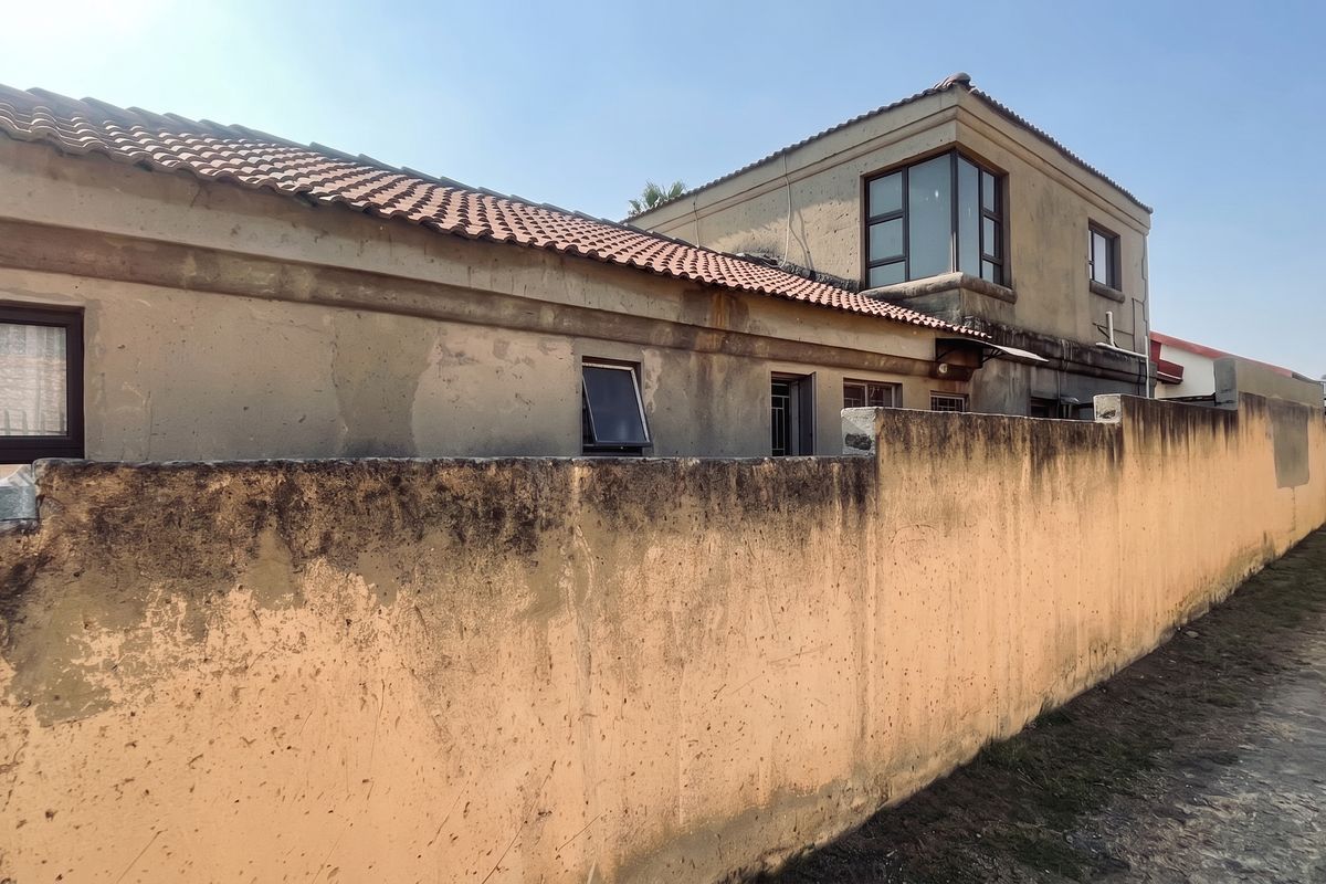 Rear exterior view of the property showing a weathered boundary wall and multi-level building structure with terracotta roof tiles.