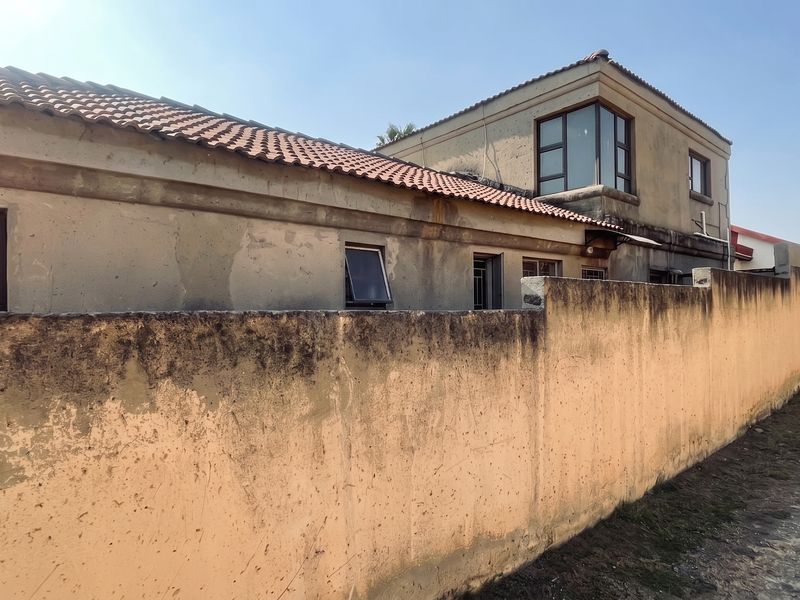 Rear exterior view of the property showing a weathered boundary wall and multi-level building structure with terracotta roof tiles.