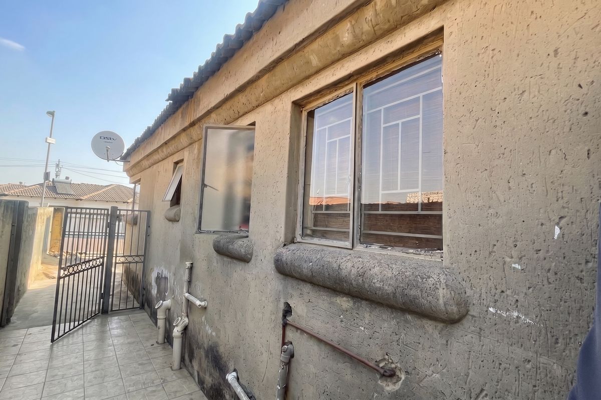 Rear exterior view of the property showing tiled walkway, security gates, and visible exterior wall maintenance requirements.