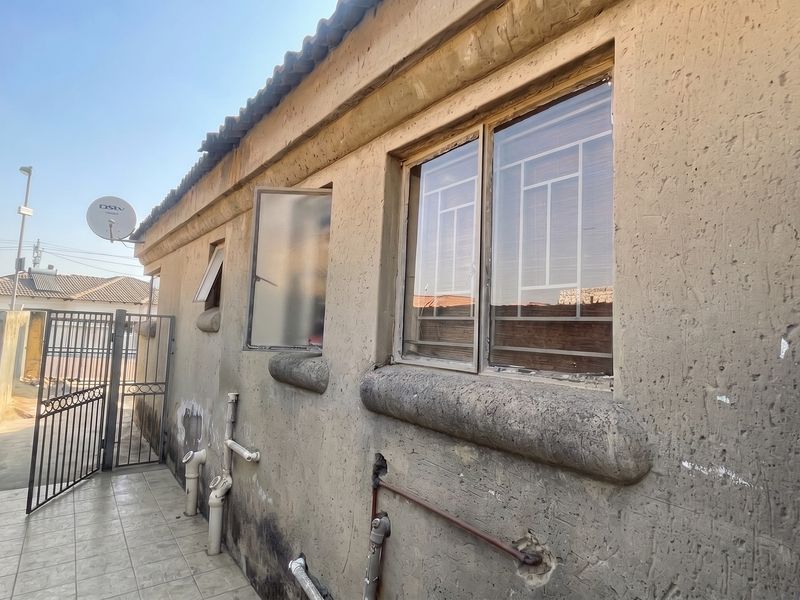 Rear exterior view of the property showing tiled walkway, security gates, and visible exterior wall maintenance requirements.