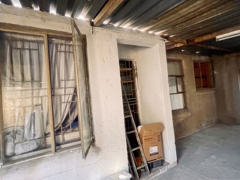 A covered outdoor patio area featuring a corrugated metal roof, timber beams, and security-barred windows, requiring maintenance and cosmetic updates.