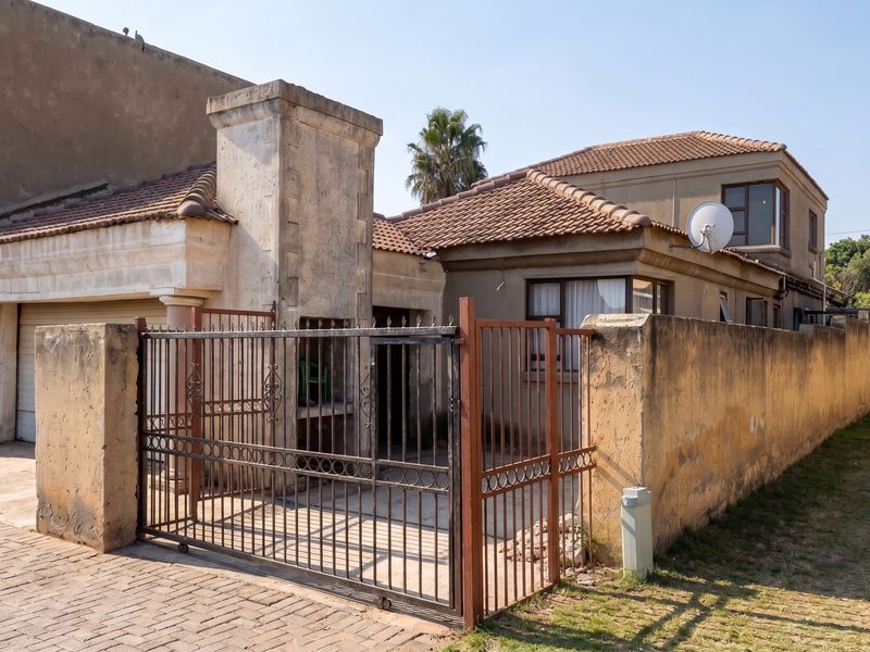 Front view of a residential property featuring a paved driveway, metal security gate, built-in outdoor fireplace, and a tiled roof structure.