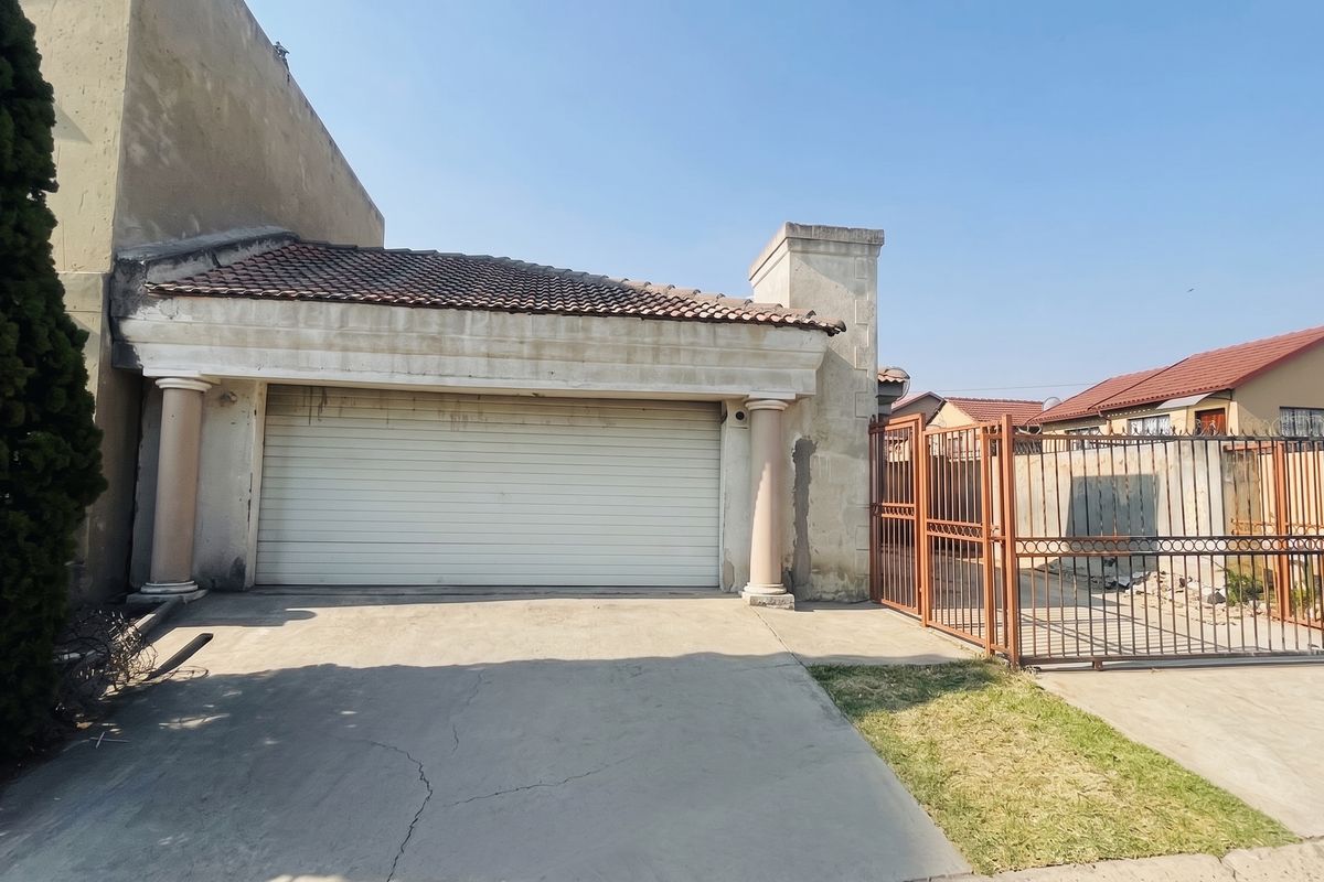Exterior view of a single garage featuring a roller shutter door, decorative columns, and a concrete driveway with an adjacent metal security gate.