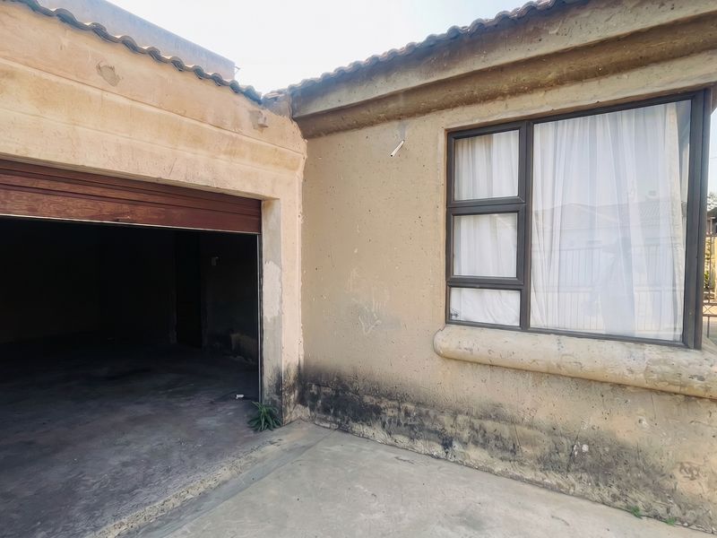 Front exterior view of the property featuring a garage entrance and a window with aluminium frames, showing significant signs of wear and weathering.