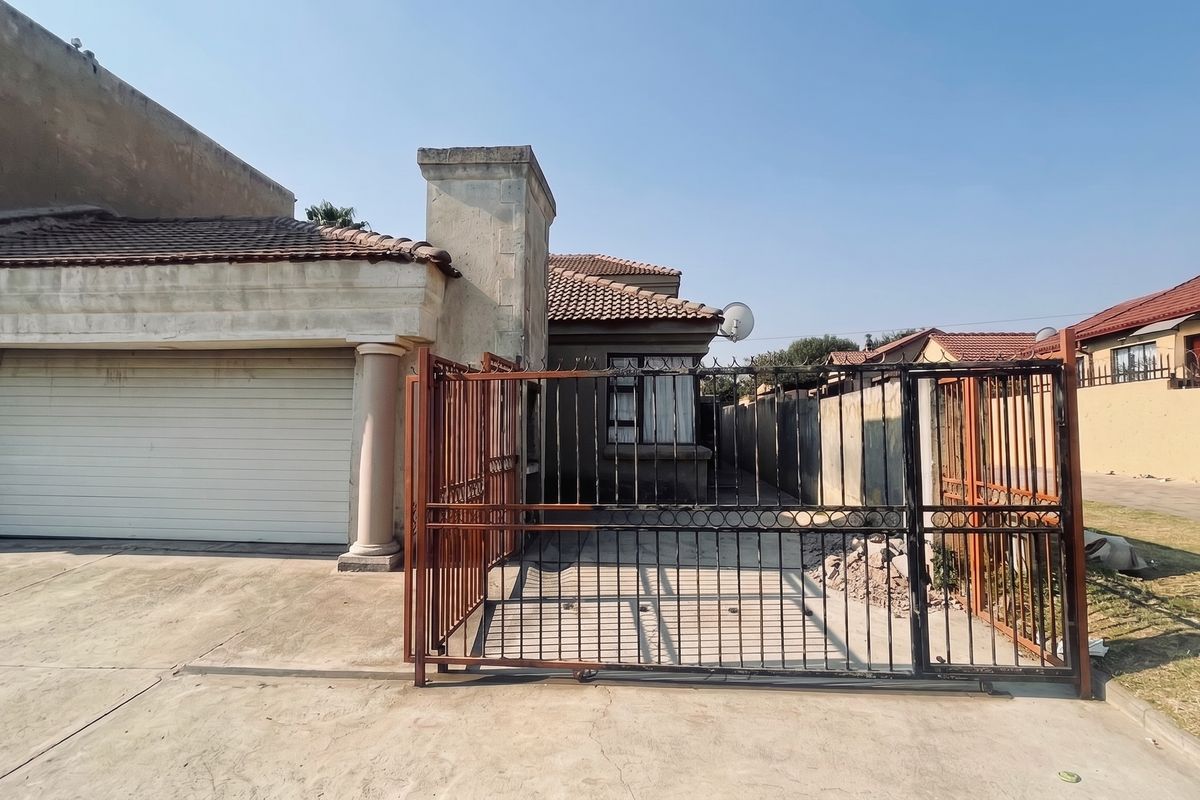 Front view of a residential property featuring a double garage, concrete driveway, and metal security gate, showing signs of exterior wear and weathering.