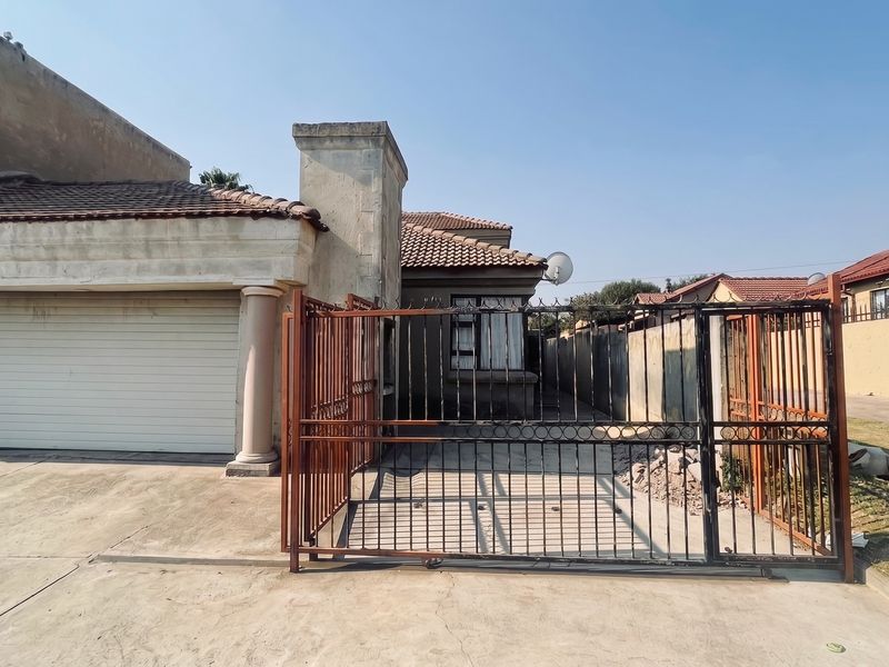 Front view of a residential property featuring a double garage, concrete driveway, and metal security gate, showing signs of exterior wear and weathering.