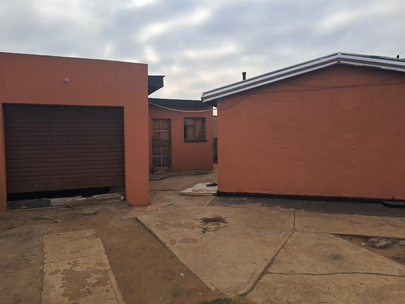 Rear exterior view of the property featuring a garage with a roller door, concrete paved yard, and basic building structures.