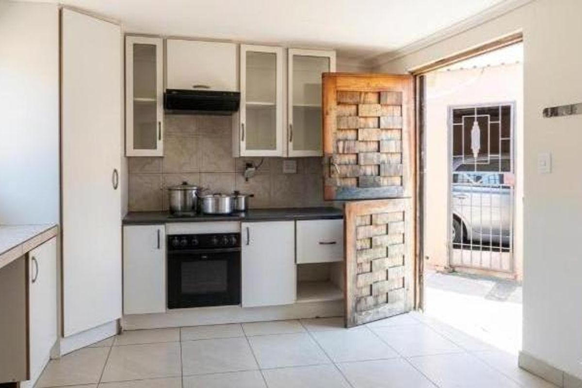 A functional kitchen featuring white built-in cabinetry, a built-in oven with extractor fan, tiled flooring, and a unique wooden stable door leading outdoors.