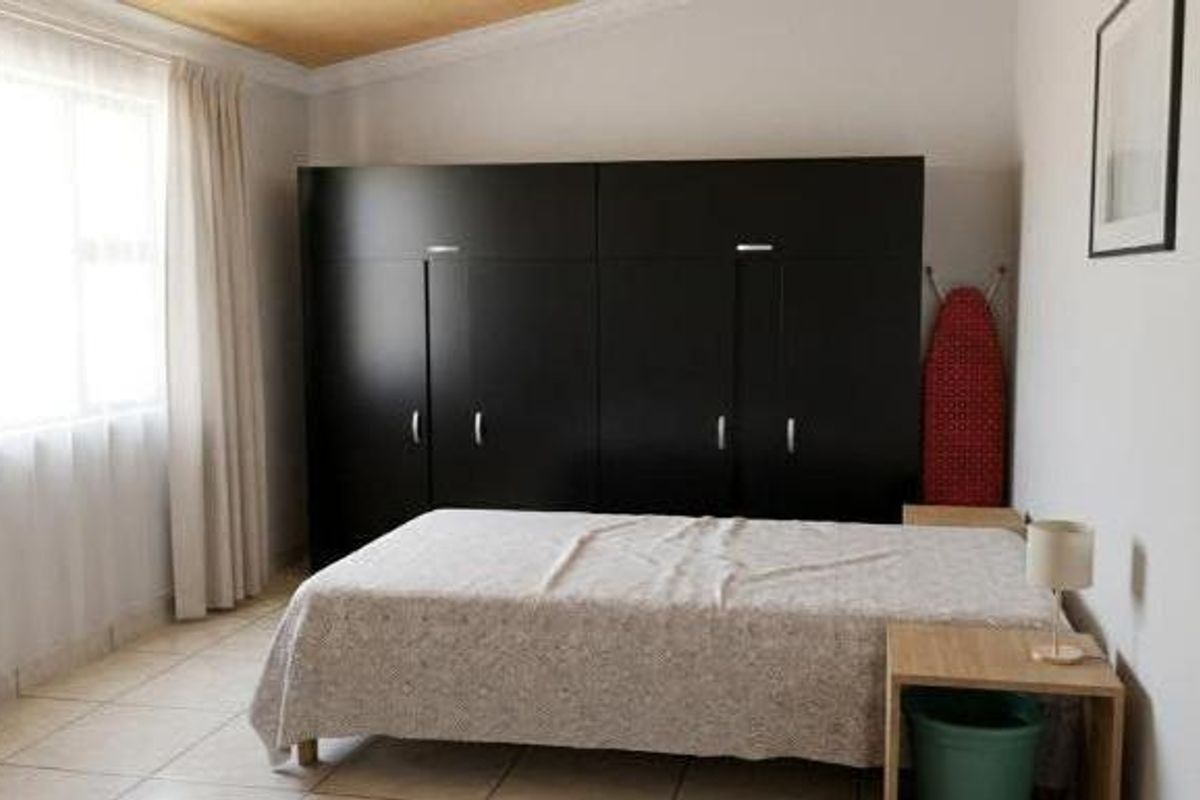 A bedroom featuring built-in cupboards, tiled flooring, and neutral wall finishes, providing a functional and well-lit living space.