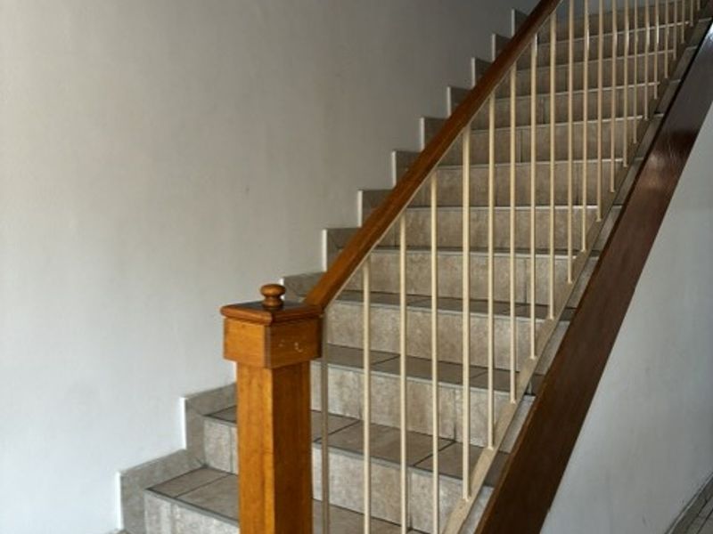 A functional staircase featuring tiled steps, a wooden handrail, and a metal balustrade, providing access between levels in the townhouse.