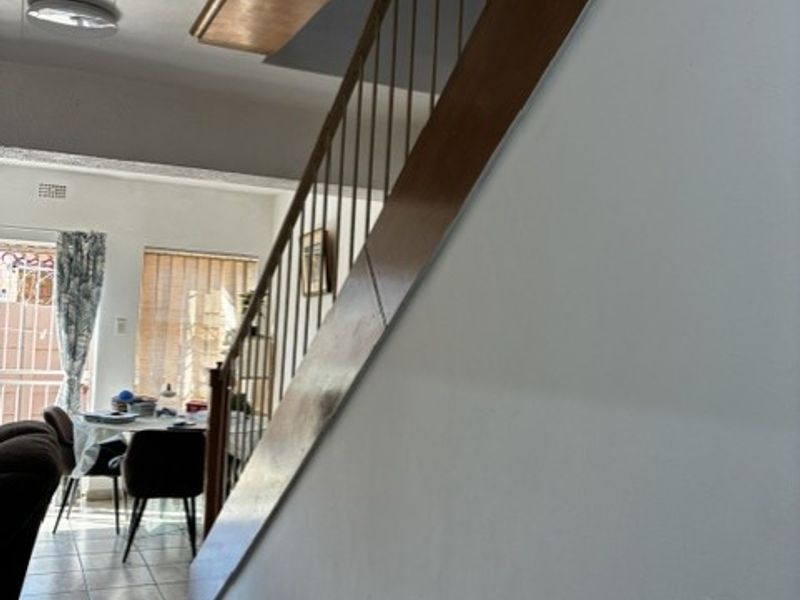A hallway area featuring a staircase with a wooden handrail and tiled flooring, leading towards an open living space.