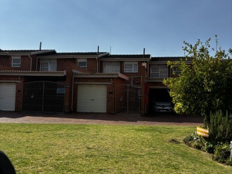 Front elevation of a multi-story townhouse complex featuring brick construction, multiple garage doors, and a well-maintained front lawn area.