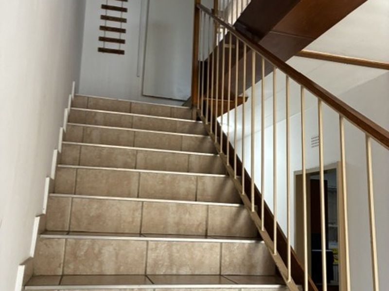 A staircase featuring tiled steps and a metal balustrade with a wooden handrail, providing access between levels in the townhouse.
