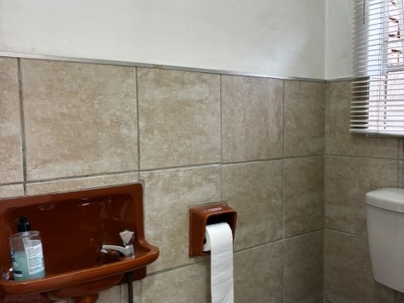 A compact bathroom featuring a wall-mounted basin, toilet, and neutral wall tiling with venetian blinds.