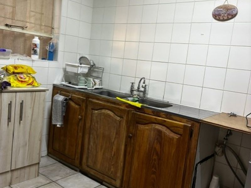 A functional scullery area featuring wooden cabinetry, a double basin sink, and tiled wall finishes, providing practical utility space for the home.