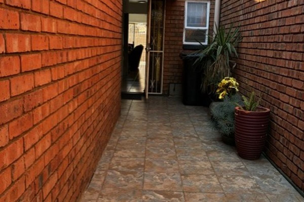 A narrow paved side passage or courtyard area featuring exposed brick walls, a small awning, and access to the interior.