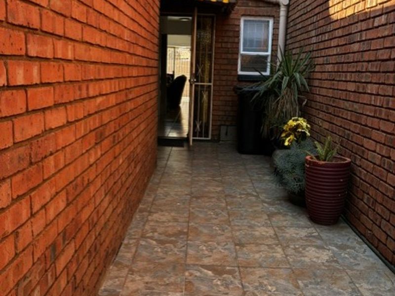 A narrow paved side passage or courtyard area featuring exposed brick walls, a small awning, and access to the interior.