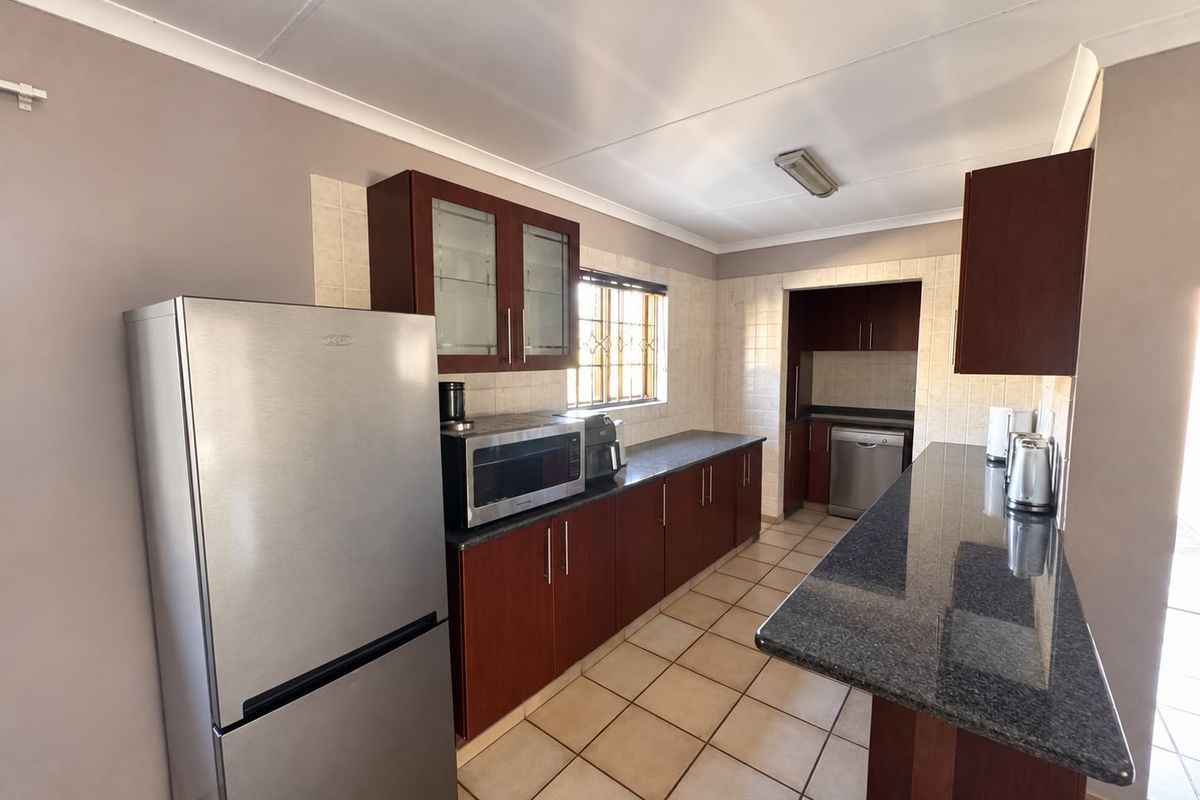 A functional kitchen featuring dark wood cabinetry, granite countertops, a breakfast bar, and tiled flooring, with a separate scullery area visible in the background.