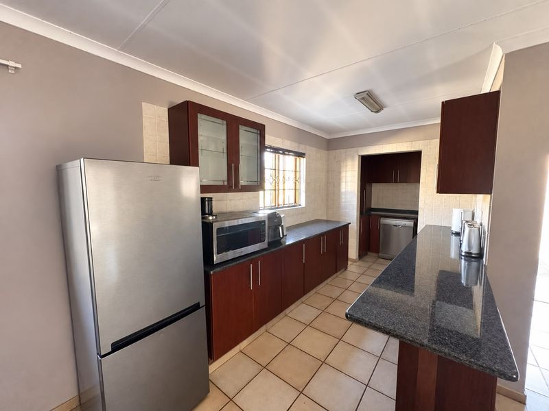 A functional kitchen featuring dark wood cabinetry, granite countertops, a breakfast bar, and tiled flooring, with a separate scullery area visible in the background.